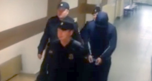 Полицейские ведут Магомеда Гучигова на заседание суда. Скриншот видеозаписи из южета телеканала НТВ, Ntv.ru/video Полицейские ведут Магомеда Гучигова на заседание суда. Скриншот видеозаписи из южета телеканала НТВ, Ntv.ru/video