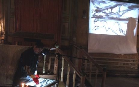 Художник Макс Эпштейн при зажженных свечах создает картины в технике документального рисования, которые под музыку в исполнении Юрия Бренера и Аркадия Шилклопера транслируются на экран проектора. Буйнакск, 8 декабря 2019 года. Фото Расула Магомедова для "Кавказского узла".