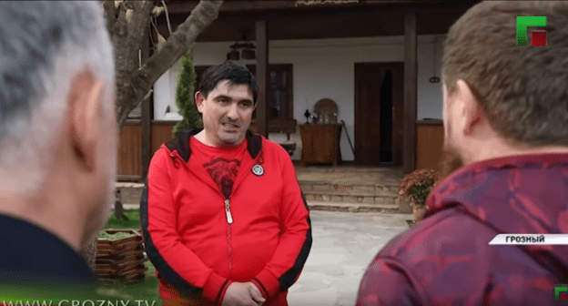 Асламбек Ахметханов (в центре) стоит перед Рамзаном Кадыровым (справа). Стоп-кадр сюжета ЧГТРК "Грозный" "Глава ЧР жестко отчитал Асламбека Ахметханова", https://youtu.be/IUHeFy2cpfk