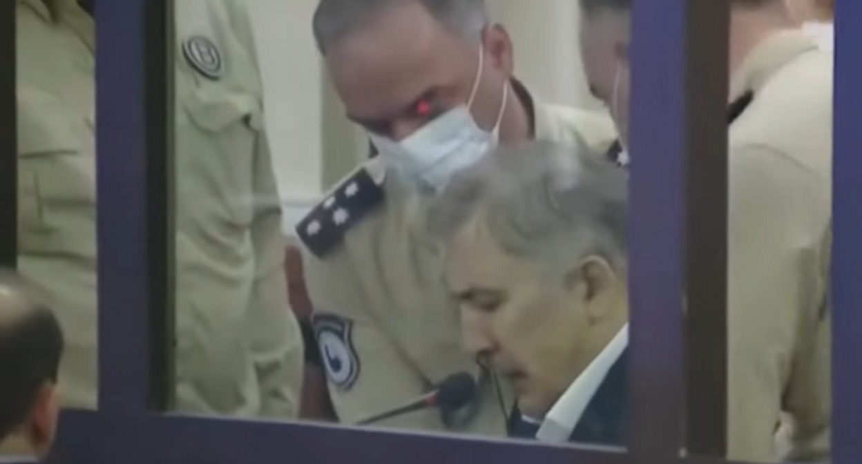 Михаил Саакашвили поднимается с места с помощью сотрудников пенитенциарной службы. Кадр сюжета Formula News www.youtube.com/watch?v=fi5Bf5740yE Михаил Саакашвили поднимается с места с помощью сотрудников пенитенциарной службы. Кадр сюжета Formula News www.youtube.com/watch?v=fi5Bf5740yE
