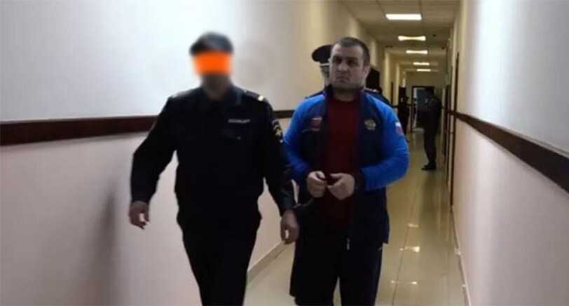 Силовики ведут Ислама Атавова. Фото: "Черновик" (лицо силовика заретушировано в исходной публикации https://chernovik.net/news/atavov-dayot-ne-sovsem-pravdivye-pokazaniya-i-vygorazhivaet-sebya-roditeli-ubitogo-v-sovetskom)