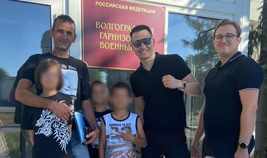 Руслан Жадаев (слева) с детьми и защитой. Скриншот фото "Высота 102" от 31.08.25, https://v102.ru/news/147301.html