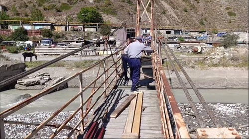 Пенсионер перешагивает незакрытый досками участок моста, не используя страховки. Кадр видеоролика из телеграм-канала ''г.п.Тырныауз. местная администрация''