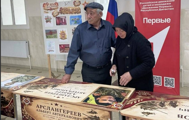 Родные на открытии именной парты. Скриншот фото администрации Бабаюртовского района от 25.05.26, https://t.me/babayurtrayon/12221?single